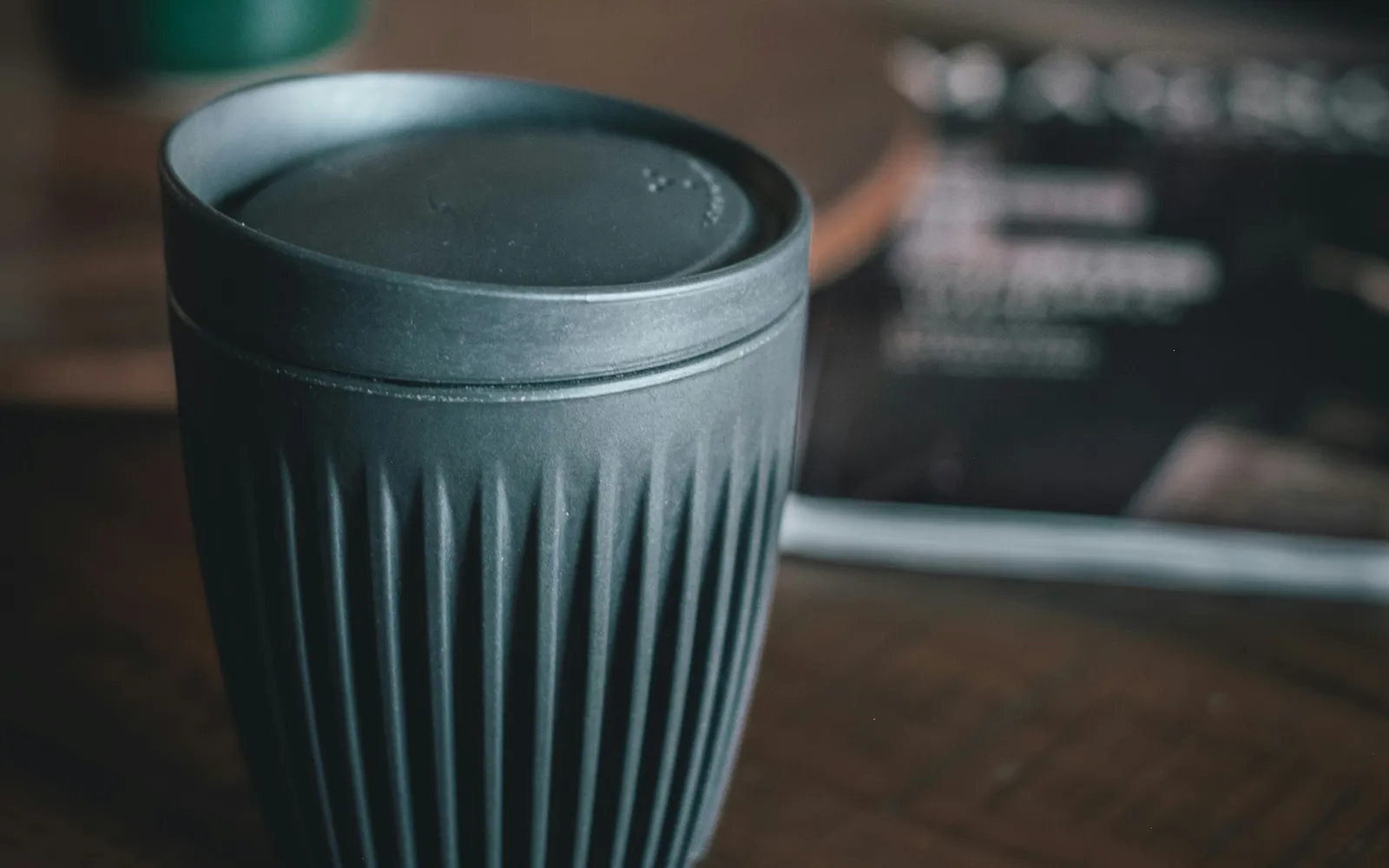 Grauer wiederverwendbarer Kaffeebecher mit gerippter Oberfläche und Deckel auf einem Holztisch