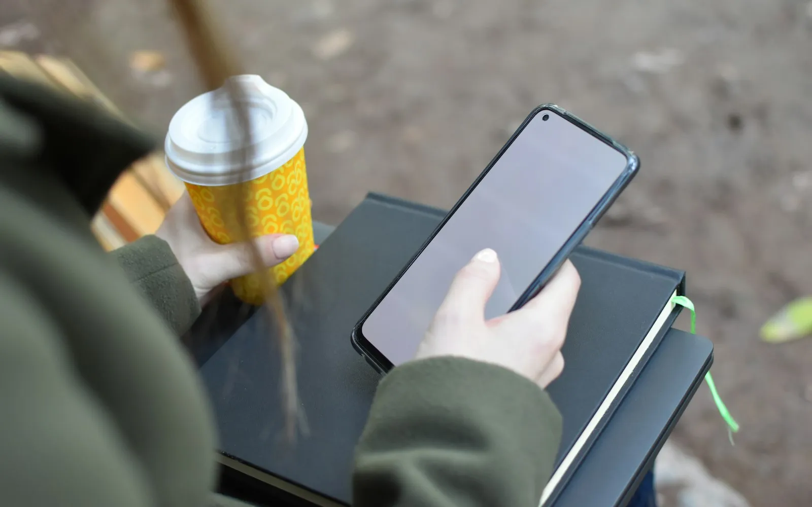 Person hält ein Smartphone und einen Kaffeebecher to go