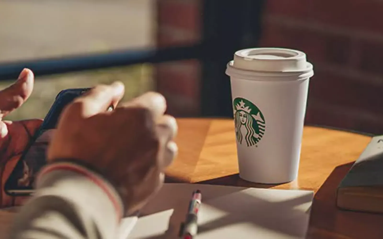 Starbucks Becher auf einem Holztisch, daneben eine Person mit Smartphone in der Hand
