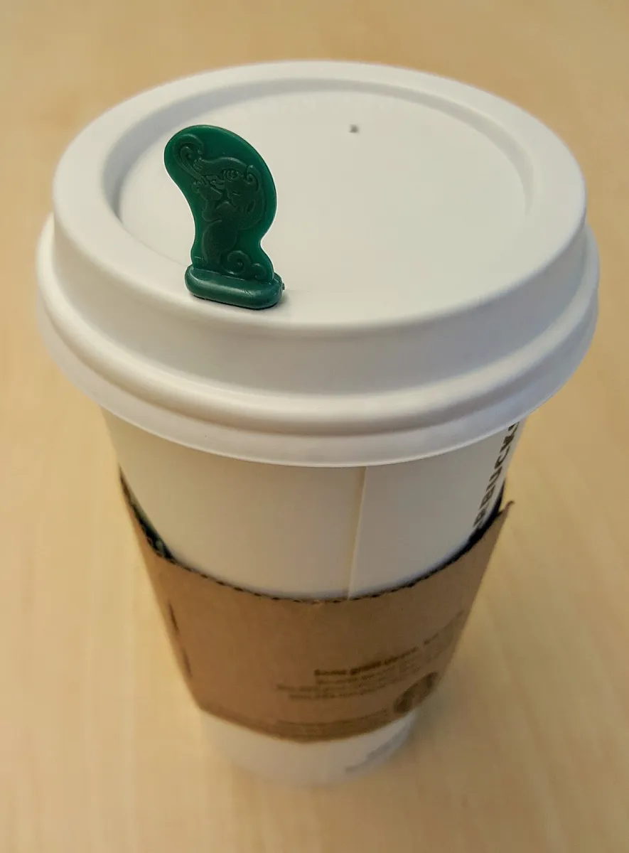 Weißer Starbucks-Pappbecher mit Kunststoffdeckel, grünem Stopper und Papphülle