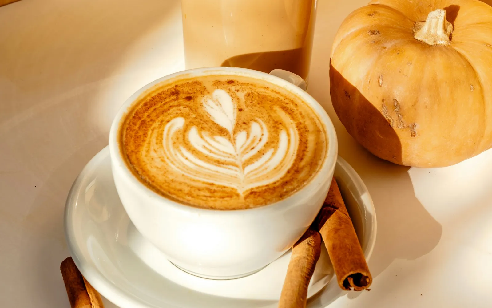 Latte mit Zimt, Latte Art und Zimtstangen neben einem kleinen Kürbis