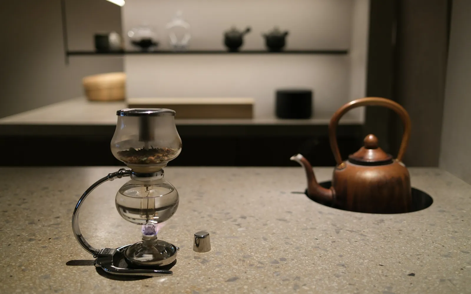Siphon-Kaffeebereiter mit Gasbrenner und Kupferkessel auf einer Steintheke